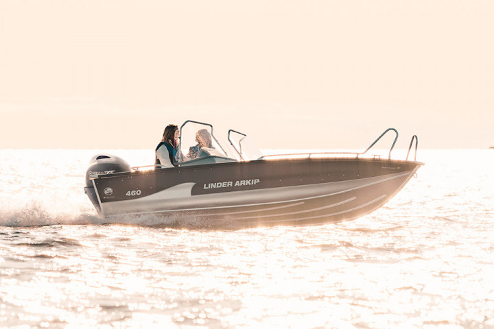 Liten motorbåt i aluminium körs av två personer på sjön en solig dag.