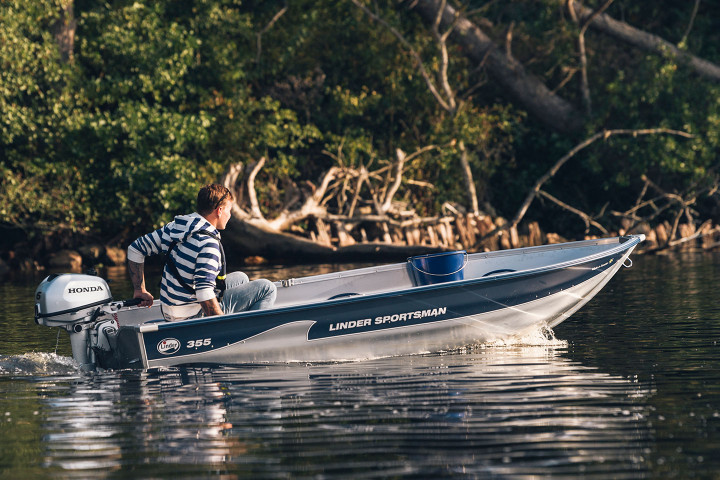 Ung tonårspojke kör båten Sportsman 355 på stilla vatten med skog i bakgrunden.