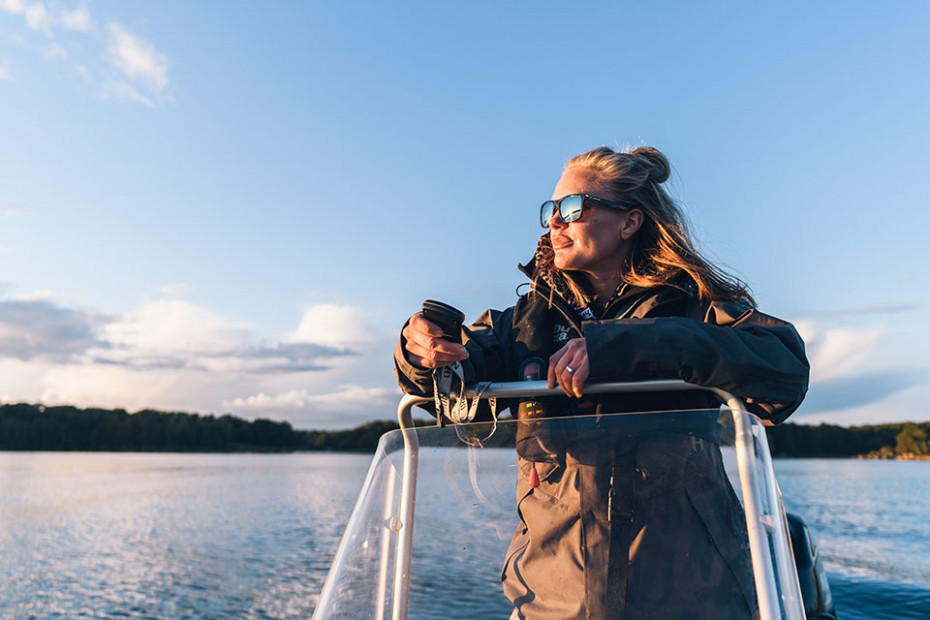 Kvinna står i sin sportfiskebåt och ser ut över vattnet en solid dag.