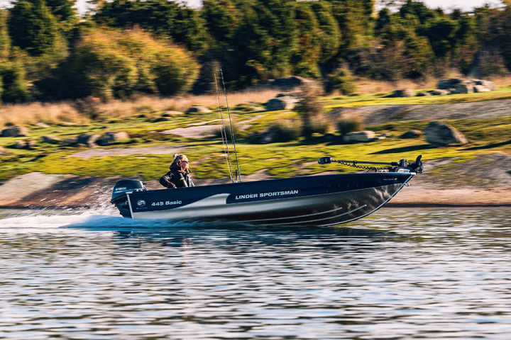 Familje- och sportbåten Sportsman 445 Basic körs fram i god fart av en person. Klippor i bakgrunden.