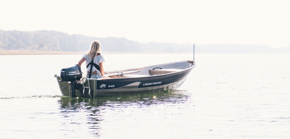En kvinna kör en Linderbåt sakta på sjön. Det är en sommarbild med mycket ljus i.