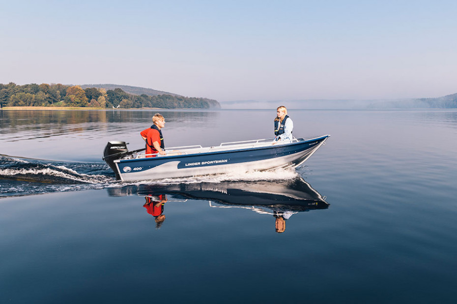 En spegelblank sjö en solig dag. Två personer kör Linderbåten Sportsman 400.