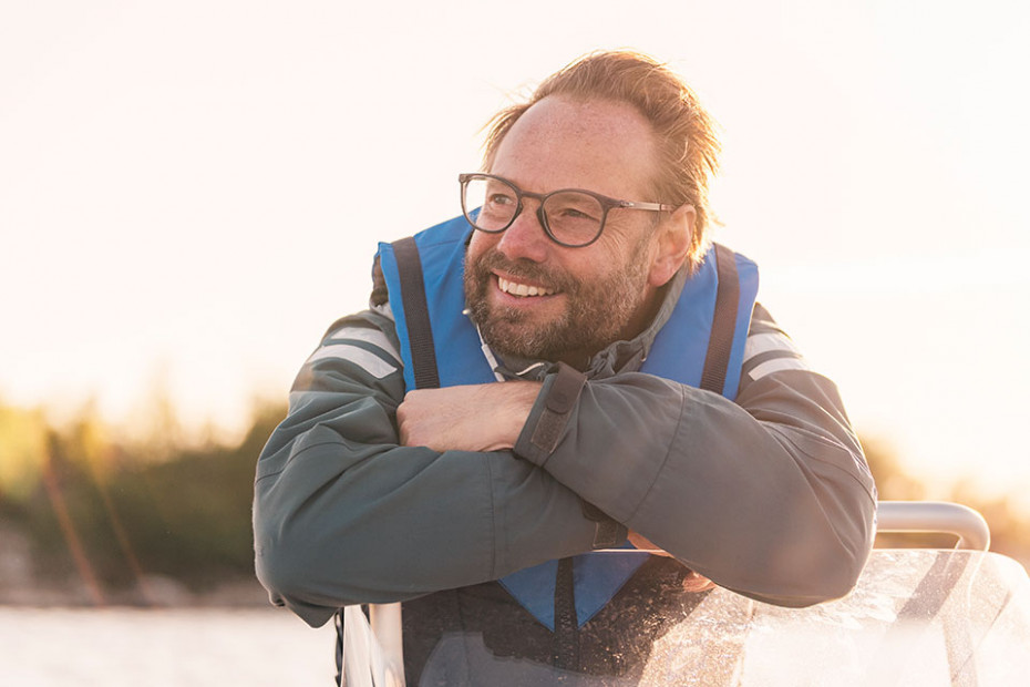En leende man i flytväst hänger med armarna över vindrutan på sin Linderbåt.
