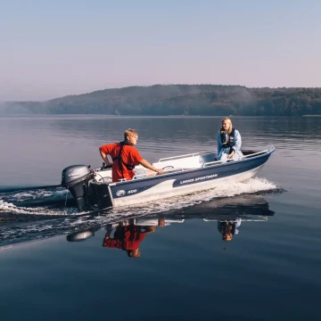 En spegelblank sjö en solig dag. Två personer kör Linderbåten Sportsman 400.