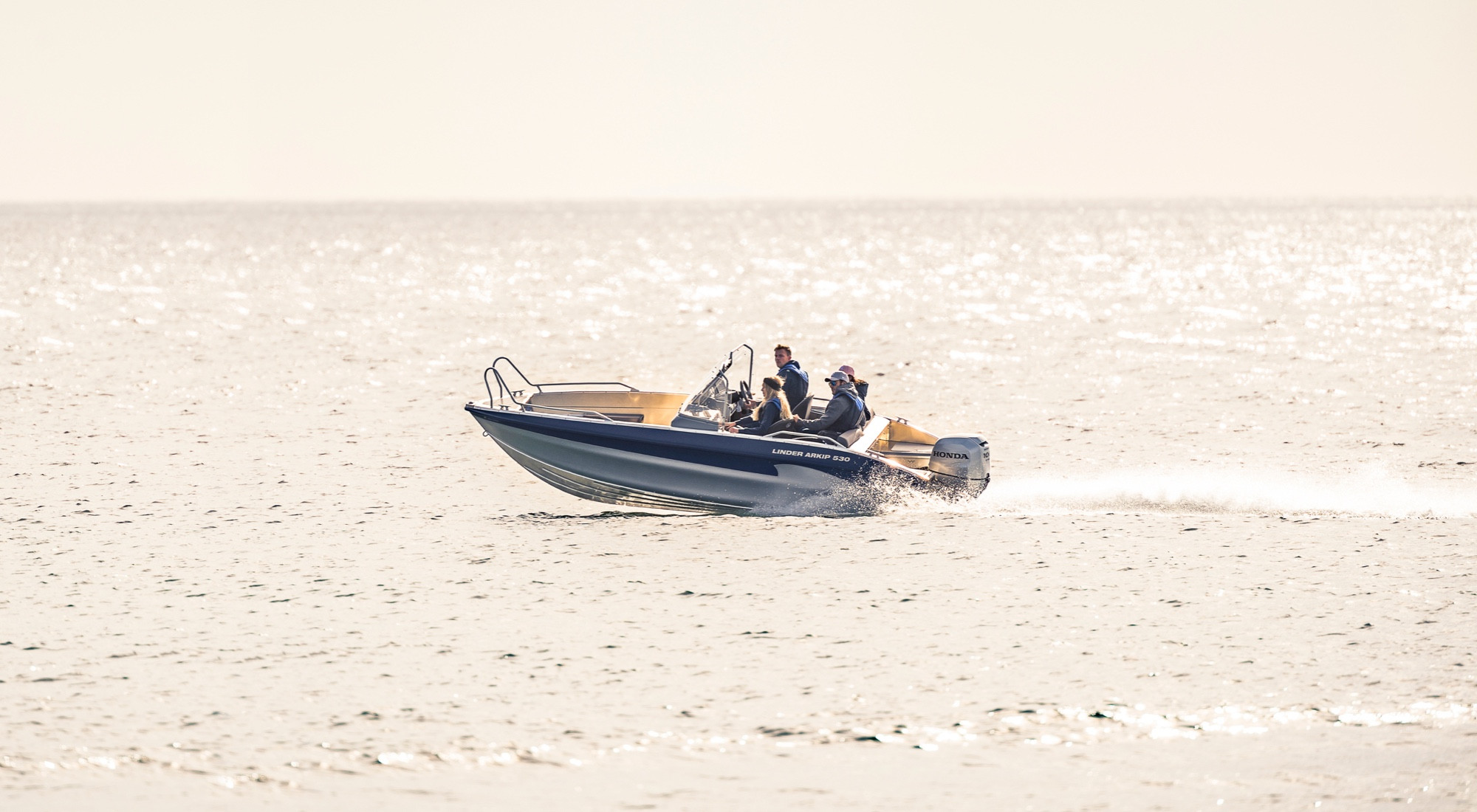 Några unga personer kör Linderbåten Arkip 530 på ett glittrande vatten i solljus.